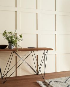 a wooden table topped with a plant and vase filled with flowers next to a white wall