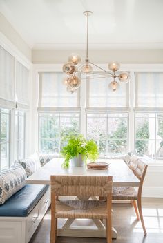 a dining room table with chairs and a bench in front of the window, next to a potted plant