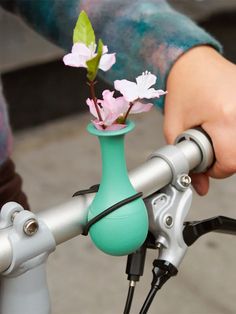 a person's hand is holding a small vase with flowers in it on the handlebars of a bicycle