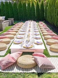 a long table set up with pink and white plates, placemats and pillows