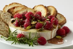 a white plate topped with bread and raspberries next to crackers on a table