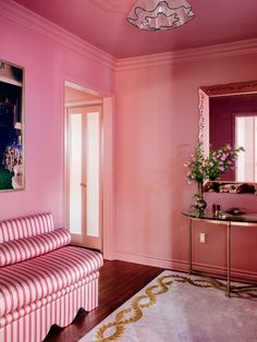 a living room with pink walls and striped couch in the corner, along with a mirror on the wall