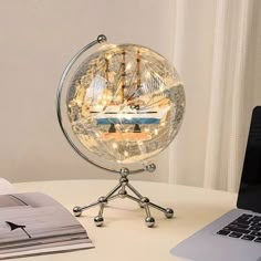 a laptop computer sitting on top of a desk next to a glass globe with a ship in it