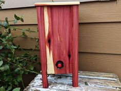 a red and white bird house sitting on top of a wooden bench next to a bush