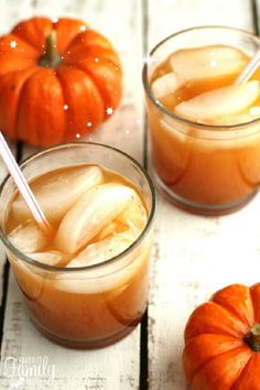 two glasses filled with pumpkin juice on top of a wooden table next to an orange pumpkin