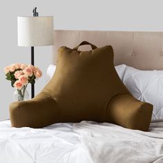 a large pillow sitting on top of a bed next to a vase filled with flowers