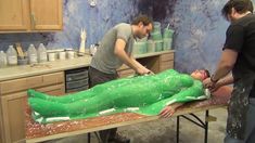 two men working on a large green object in a room with wooden cabinets and counter tops