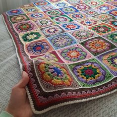 someone is holding up a crocheted granny's square blanket on the floor