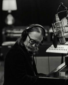 a man with headphones on sitting at a piano in front of a microphone and recording equipment