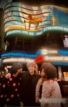 three people standing in front of a large building with billboards on it's side