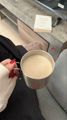 a woman is holding a cup of coffee in her hand while sitting on a couch