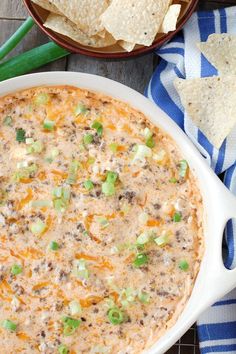 a white casserole dish filled with cheese and green onions next to tortilla chips