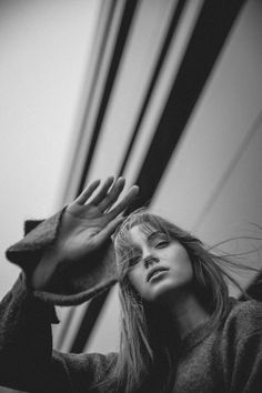 a black and white photo of a woman with her hands on her head, leaning against a wall