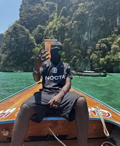 a man sitting on the back of a boat holding a drink in his hand while wearing a mask