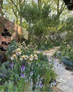 a garden with lots of flowers and trees in the background, surrounded by stone walkways