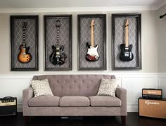 three guitars are hanging on the wall above a couch in front of two amps