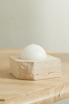 a white candle sitting on top of a block of concrete next to a wooden table