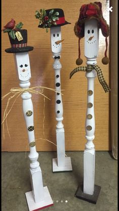 three white candlesticks decorated to look like snowmen with hats and bows on their heads