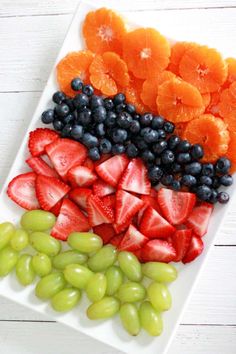 grapes, strawberries, and oranges are arranged on a white platter to look like an american flag