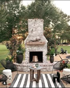 an outdoor fireplace with potted plants and chairs around it on a striped area rug