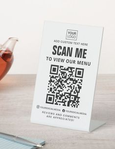 there is a sign that says scan me to view our menu on the table next to a cup of tea