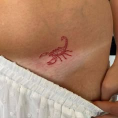 a woman's stomach with a small red scorpion tattoo on it