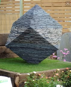 a stone sculpture sitting on top of a lush green field next to a wooden fence