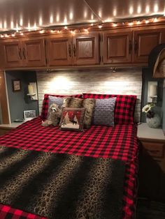 a bed with red and black plaid comforter in a room filled with wooden cabinets