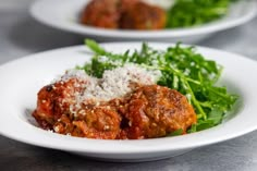 two white plates topped with meatballs covered in parmesan cheese and lettuce