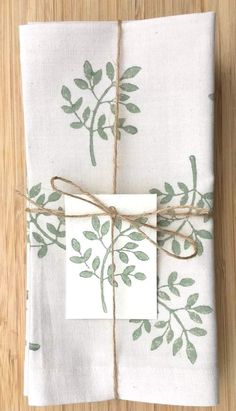 two napkins tied up with twine on top of each other, both decorated with green leaves