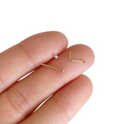 a person's hand holding two small gold nose rings with tiny diamonds on them