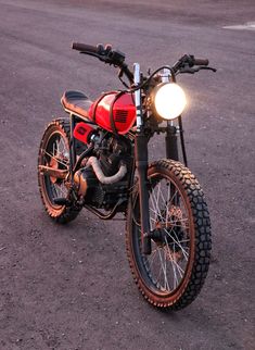 a red and black motorcycle parked on top of a dirt covered field next to a parking lot