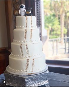 a three tiered white cake sitting on top of a silver table next to a window