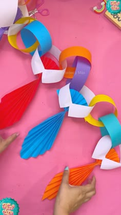 someone is making colorful paper chains on a pink surface with scissors and other crafting supplies