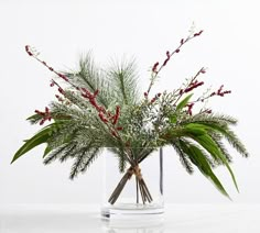 a glass vase filled with lots of greenery and red berries sitting on top of a table