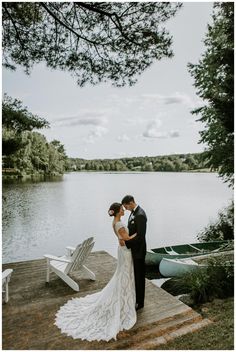 a bride and groom standing on a dock by the water in front of canoes