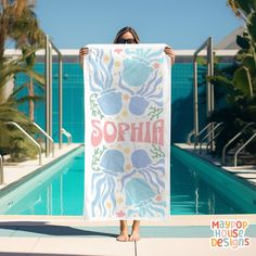 a woman is holding up a towel with the word sophia on it in front of a swimming pool