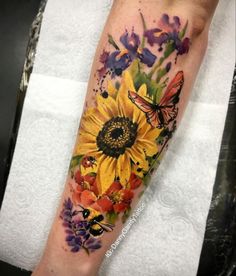 a sunflower and butterfly tattoo on the arm with watercolors in it's center