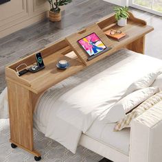 a bed with a laptop on top of it next to a table that has a phone and other items