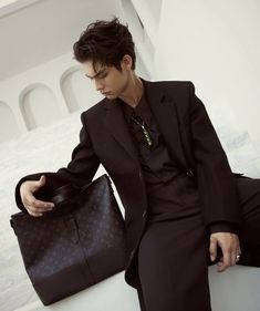 a man in a suit and tie sitting on a ledge holding a black handbag