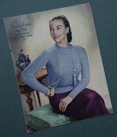 an old photo of a woman sitting on a chair wearing a blue sweater and purple skirt