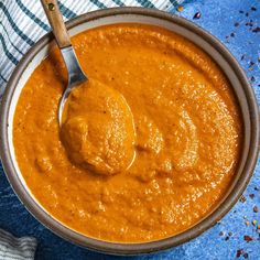 a spoon in a bowl filled with red sauce on top of a blue table cloth