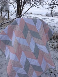 a pink and grey quilt sitting on top of a snow covered ground next to a tree