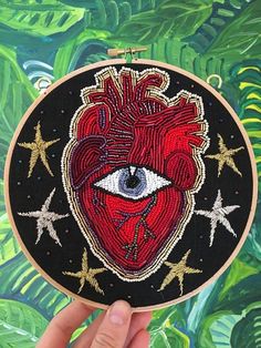 someone is holding up a hand embroidered heart with an eye