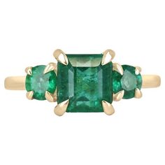 Indulge in the timeless elegance of our Emerald Trilogy Three Stone Ring, where a captivating asscher-cut emerald takes center stage, flanked by two round cut emeralds to create a stunning trilogy. All three gemstones showcase a mesmerizing lush green color with semi-transparent clarity, evoking a sense of natural sophistication. Expertly set in a four-claw prong setting crafted from radiant 14k yellow gold, this ring is a harmonious blend of classic design and vibrant allure. Setting Style: Pro Claw Prong, Asscher Cut, Yellow Gold Setting, Semi Transparent, Three Stone Rings, Center Stage, Lush Green, Jewelry Rings Engagement, Three Stone