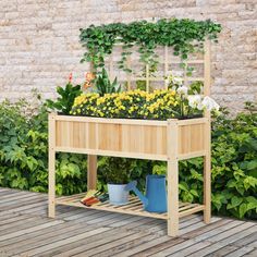 a wooden planter filled with lots of flowers next to a brick wall and shrubbery