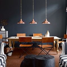 a dining room with black walls and wooden table surrounded by striped chairs, vases and hanging lights