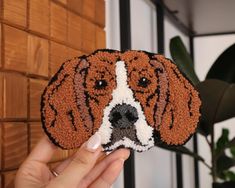 a hand holding up a brown and white beaded dog ornament in front of a brick wall