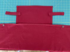 two pieces of red fabric sitting on top of a blue cutting mat next to a pair of scissors