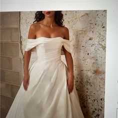 a woman in a white dress standing next to a brick wall